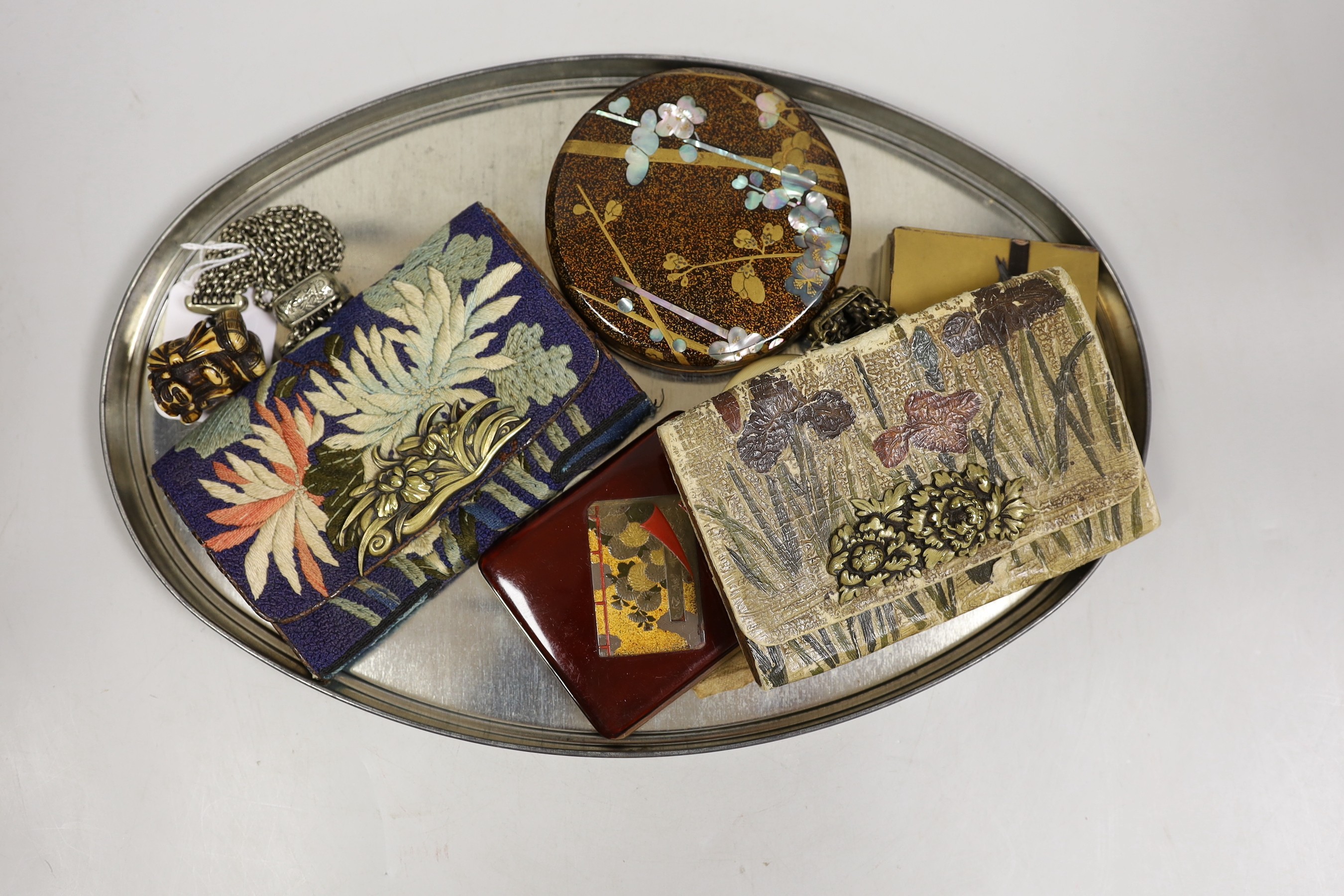 Two crepe paper Japanese illustrated books, a Japanese enamel compact two lacquer boxes and covers and two Japanese tobacco pouches, one with ivorine manju netsuke and the other a carved staghorn netsuke of Daikoku